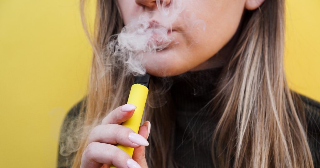 A,Young,Girl,Smokes,Disposable,Electronic,Cigarette.,Bright,Yellow,Background